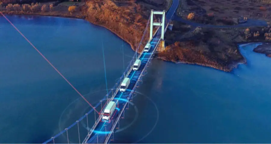 Connected fleet of trucks driving on a high-tech bridge with digital overlay representing IoT and supply chain management for Banyan Technology.