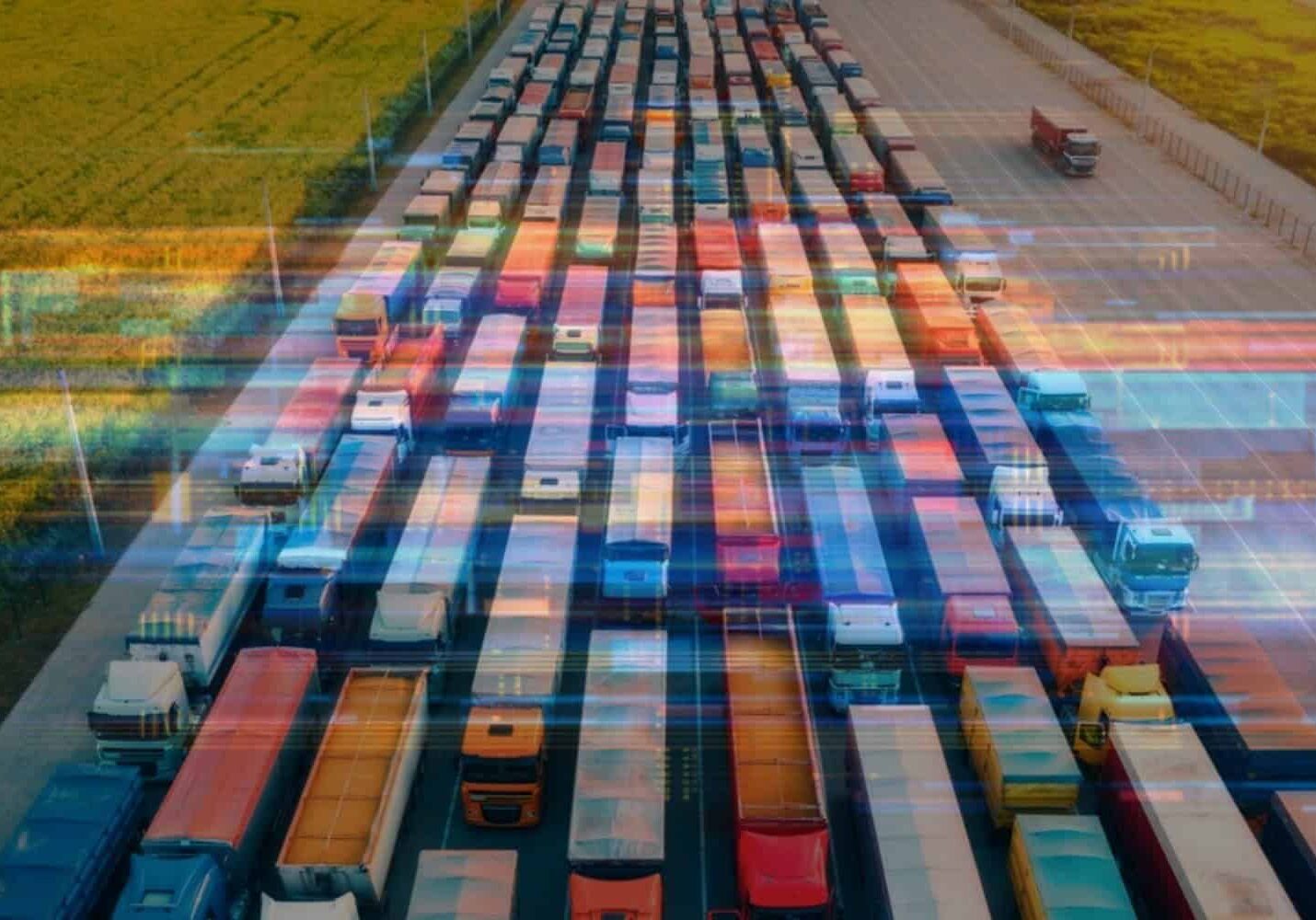 A variety of over-the-road freight trucks driving through a shipping hub