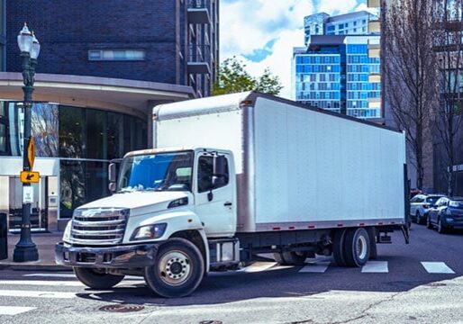 White delivery truck parked on city street near modern office buildings, illustrating efficient logistics and supply chain solutions for businesses.